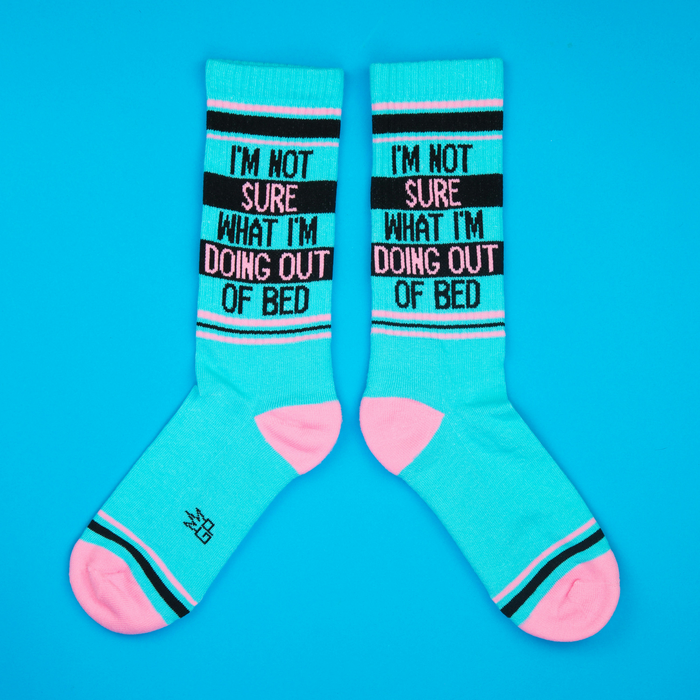 Flat lay of teal 'I'm Not Sure What I'm Doing Out Of Bed' socks against a bright blue background.
