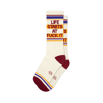 Pair of cream crew socks with maroon, gold, and purple stripes and the phrase 'Life Starts At Fuck It' in a retro font.