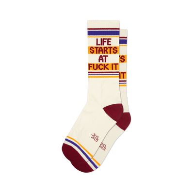 Pair of cream crew socks with maroon, gold, and purple stripes and the phrase 'Life Starts At Fuck It' in a retro font.