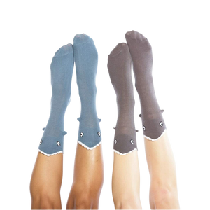 A pair of gray socks with a shark face on each sock. The shark face has a black nose and mouth and a white tooth. The socks are mid-calf length and have a scalloped edge at the top.