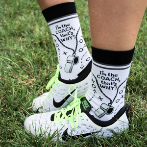 Lifestyle shot of 'I'm the Coach' socks on feet wearing athletic shoes, outdoors on grass.