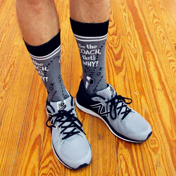 [lf] Lifestyle shot of 'I'm the Coach' socks worn with gray athletic shoes on a wood floor.