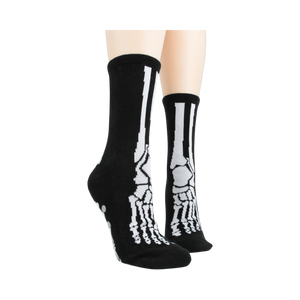 Lifestyle shot of model wearing black skeleton socks with grey non-skid bottoms against a black background.