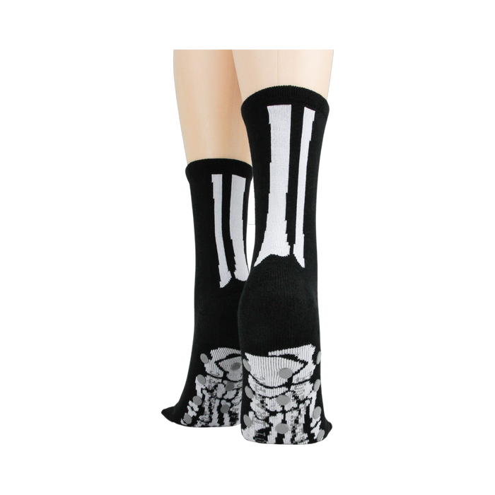 Rear view of model's legs wearing black skeleton socks with grey non-skid bottoms against a black background.