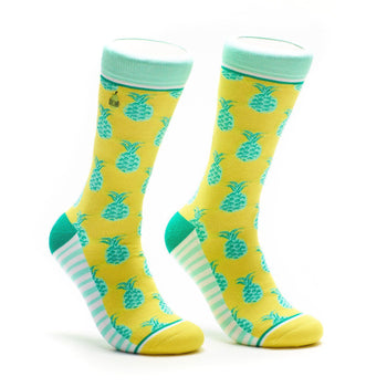 A pair of crew socks in yellow with teal pineapples. The cuffs are mint green and white stripes accent the heel and toe.
