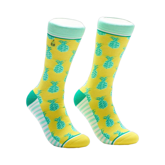 A pair of crew socks in yellow with teal pineapples. The cuffs are mint green and white stripes accent the heel and toe. }}