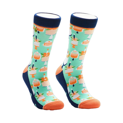 A pair of crew socks with a mint green background and repeating pattern of orange cakes with candles. The socks have navy blue cuffs and orange toes.
