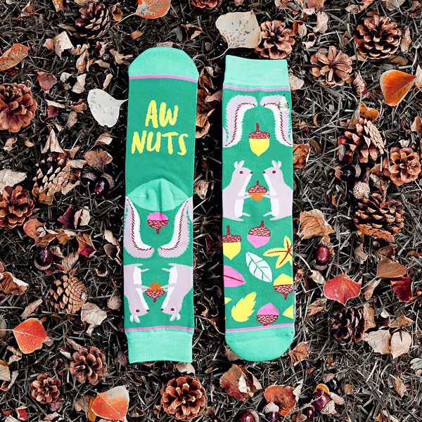 Lifestyle shot of 'Aw Nuts' socks on a bed of autumn leaves and pine cones. [lf]