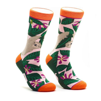 A pair of crew socks with a pink, green, and orange design.  The socks feature sloths hanging from tropical leaves and flowers.