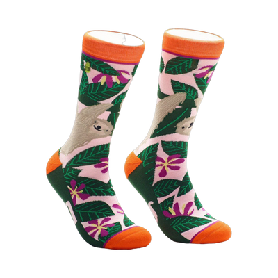 A pair of crew socks with a pink, green, and orange design.  The socks feature sloths hanging from tropical leaves and flowers.