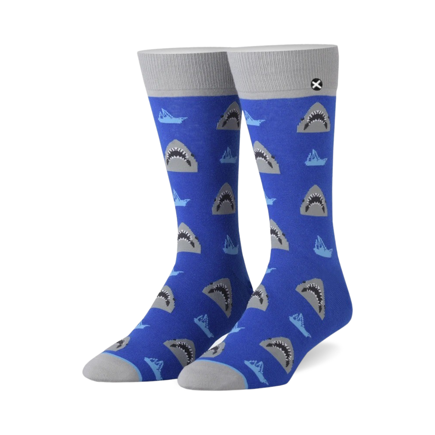 A pair of blue crew socks with a repeating pattern of grey shark faces and small, light blue boats.  The socks have grey cuffs.