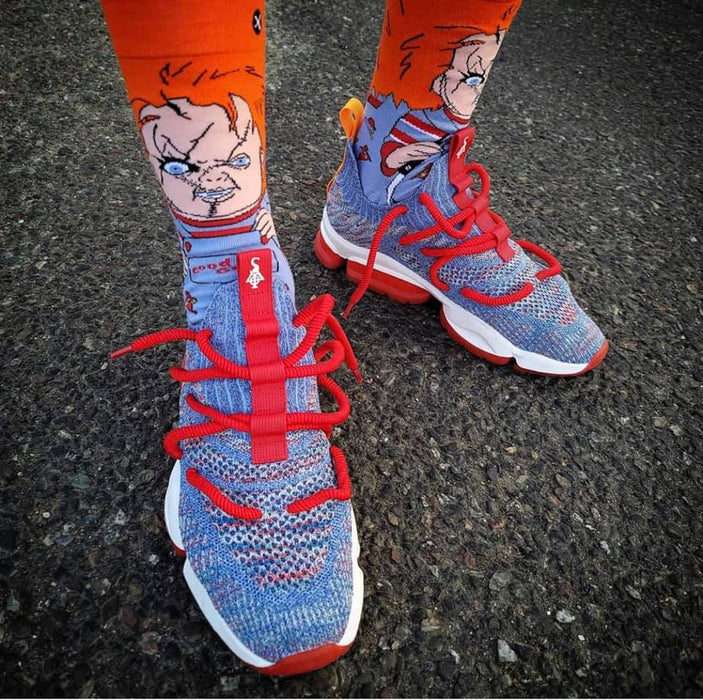 A person is wearing a pair of blue and orange sneakers with red laces. The socks are orange with a picture of Chucky from the horror movie series 
