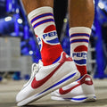 Person wearing Pepsi Throwback crew socks and white sneakers with red and blue accents, standing on concrete. [lf]