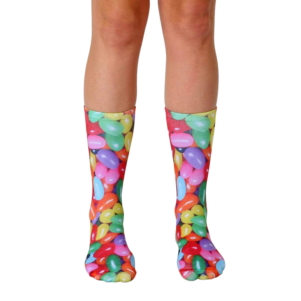 A pair of crew socks with a colorful jelly bean print.  The socks feature red, yellow, green, purple, and orange jelly beans on a white background. [lf]
