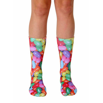 A pair of crew socks with a colorful jelly bean print.  The socks feature red, yellow, green, purple, and orange jelly beans on a white background.