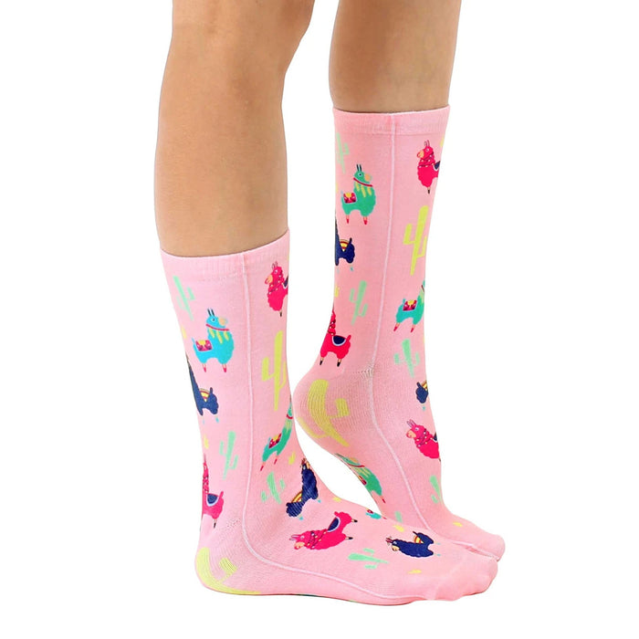A pair of pink socks with a pattern of llamas wearing colorful saddles and bridles.