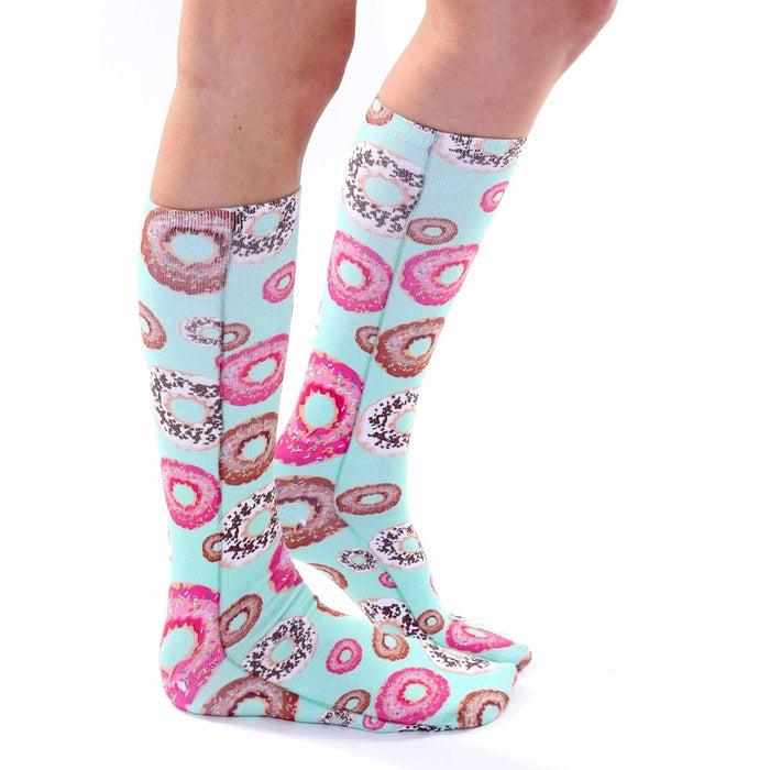 A pair of legs is shown from the knees down. The person is wearing a pair of knee-high socks with a pattern of doughnuts on a mint green background.