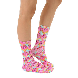 A pair of legs is shown from the knee down. The person is wearing pink socks with a pattern of blue icing donuts with pink sprinkles.