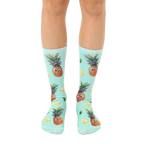 A pair of mint green crew socks with a fun all-over print of googly-eyed pineapples and pineapple wedges. [lf]