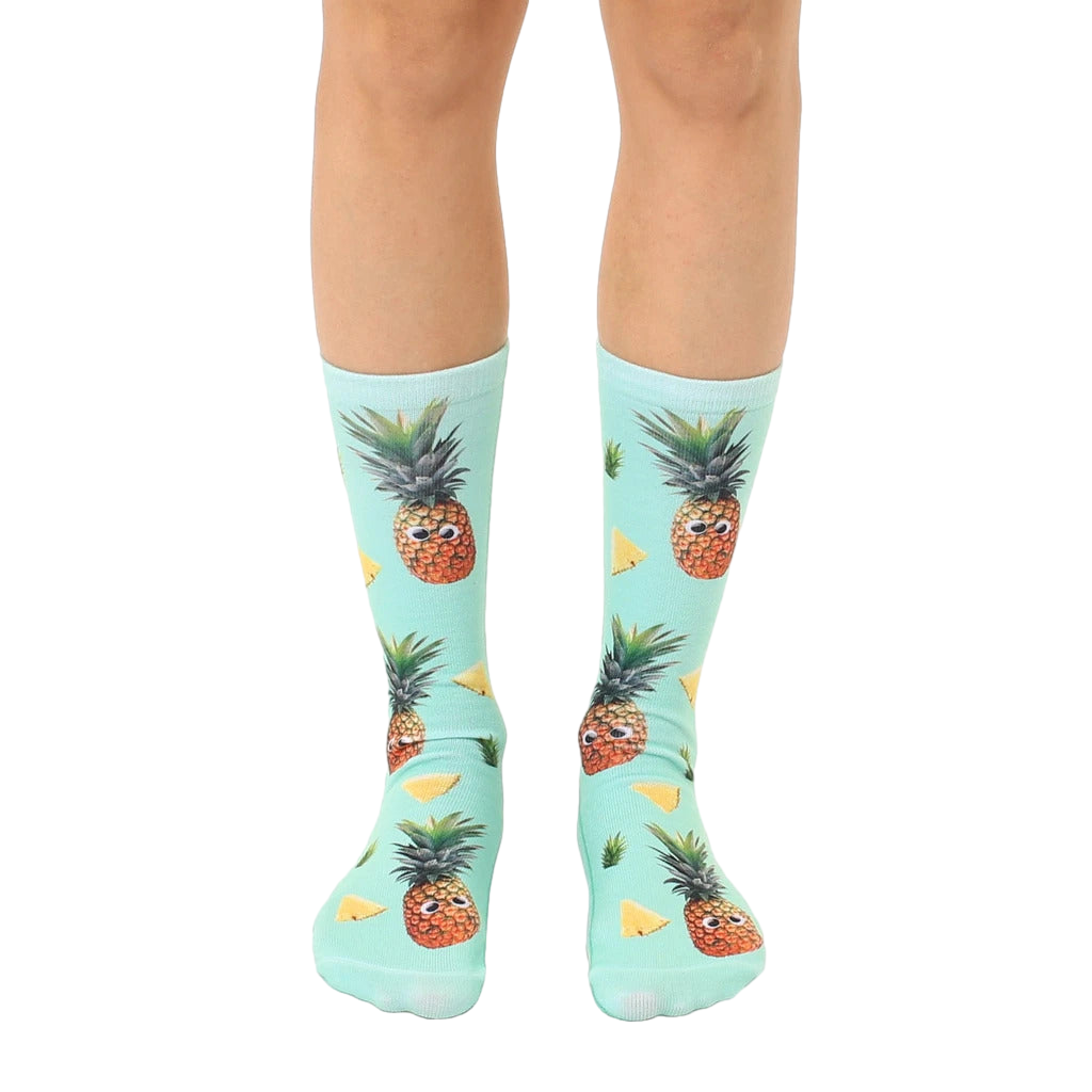 A pair of mint green crew socks with a fun all-over print of googly-eyed pineapples and pineapple wedges. [lf]