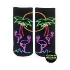 Pair of black ankle socks with a neon glow-in-the-dark design. Flamingos, palm trees, and a sunset are depicted in pink, purple, and green.