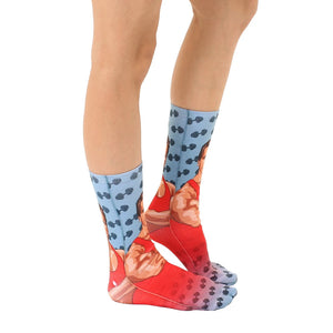 A pair of socks with a photo of Arnold Schwarzenegger in a red tank top on a blue background. The socks also have barbells on a light blue background.