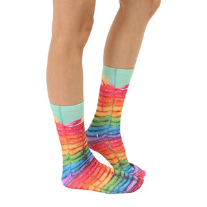 A person's feet are shown wearing rainbow-colored socks that have a photo print of a stack of pancakes with syrup on them.