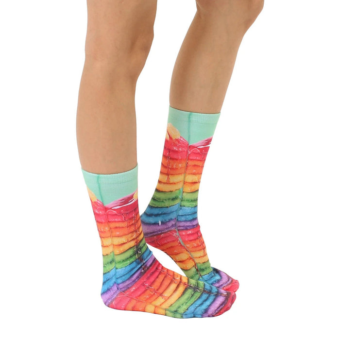 A person's feet are shown wearing rainbow-colored socks that have a photo print of a stack of pancakes with syrup on them.