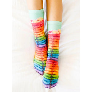 A person's feet are shown wearing rainbow-colored socks that have a photo print of a stack of pancakes with syrup on them.