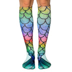 Pair of rainbow mermaid scale knee-high socks. Teal mermaid tail at the bottom.  Colorful, whimsical design. [lf]