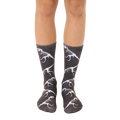 A pair of crew socks on a person's legs. The dark grey socks feature a repeated pattern of white T-Rex dinosaur skeletons. [lf]