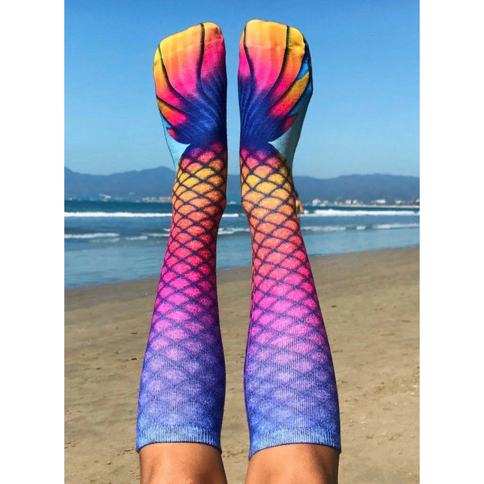 A pair of blue, pink, and purple mermaid tail socks with a scale pattern and yellow, orange, and pink fin design at the top.