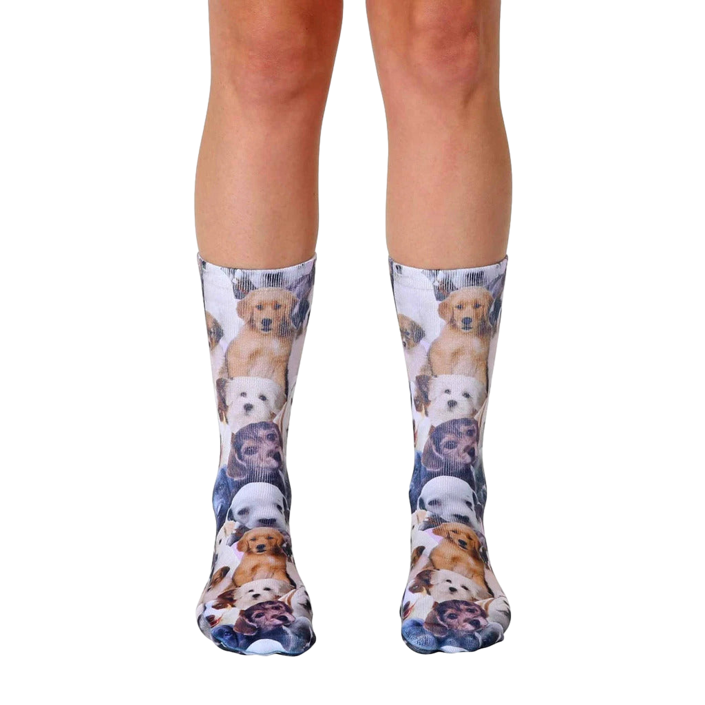 A pair of crew socks covered in an all-over print of adorable puppies in various breeds and colors. The socks are mainly white with brown, tan, and black puppies. [lf]
