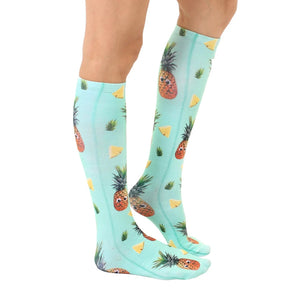 A pair of knee-high socks with a pattern of pineapples on a mint green background.