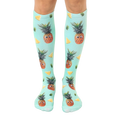 Pair of knee-high socks. Teal background with repeating pattern of cartoon pineapples with googly eyes and pineapple slices. [lf]