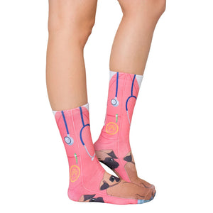 A person is shown wearing a pair of pink socks that have an image of a cartoon pug wearing a stethoscope and a pink scrub top on them.