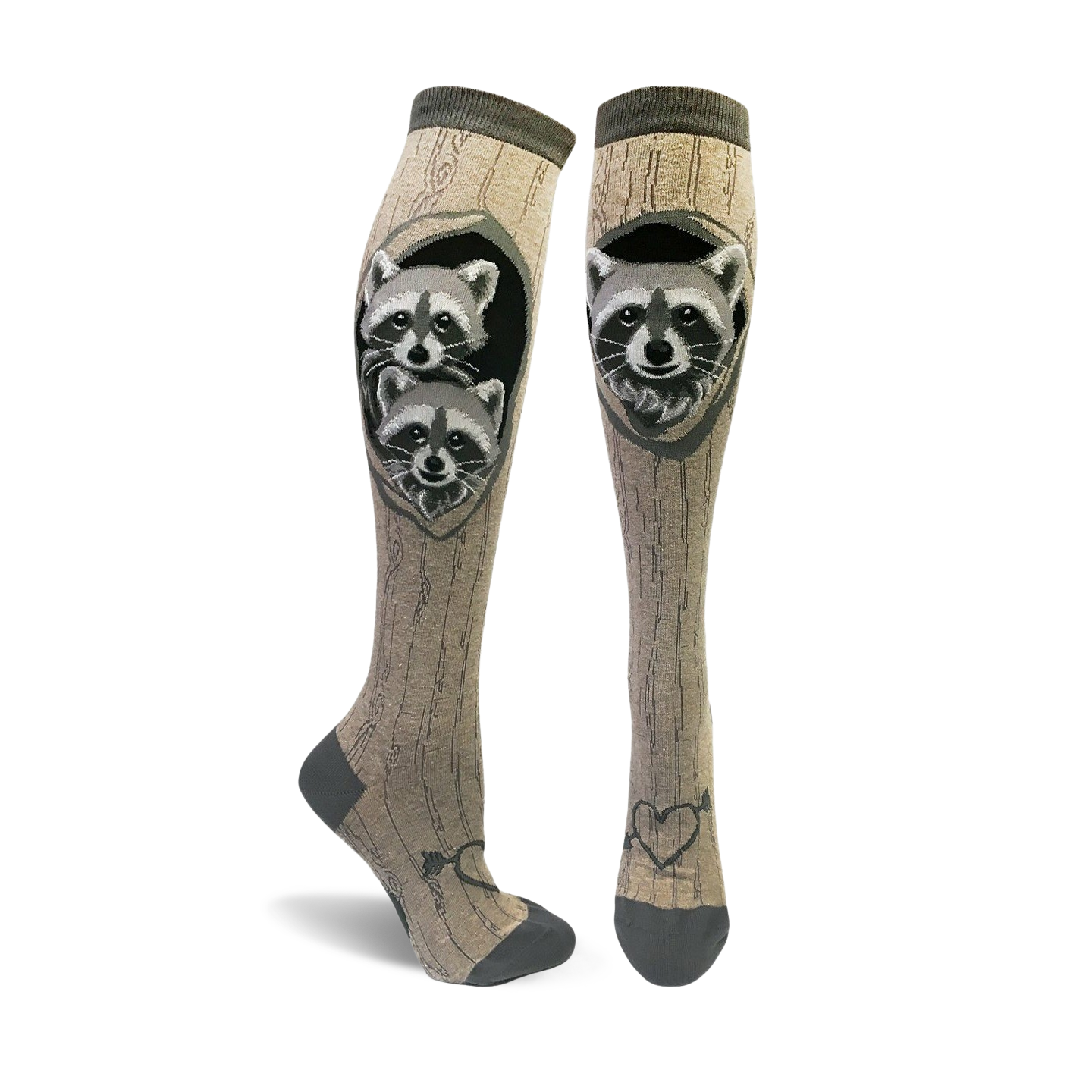 A pair of tan knee-high socks with a wood grain pattern and two raccoons peeking from a tree hole.  The socks have dark gray toes and heels, and a small heart with arrow detail at the ankle.