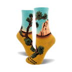 A pair of women's crew socks showcasing a Joshua Tree National Park design. The socks are teal and mustard yellow, depicting a desert landscape with iconic Joshua trees and rock formations.
