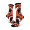 Crew socks in orange and purple featuring black cats perched on skulls beneath a crescent moon. Ornate detailing.