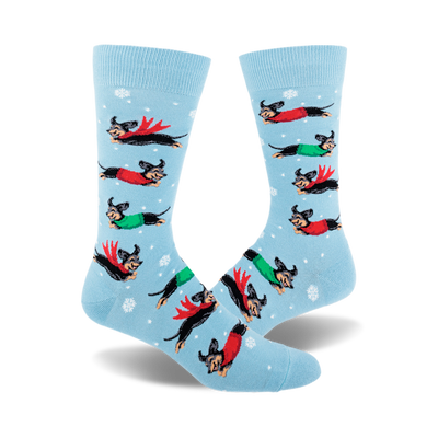 front view of men's crew socks; sky blue background with dachshunds wearing winter clothes, leaping through snowflakes.