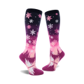 Pair of women's knee-high socks. Pink and purple ombre design with white snowflakes and a winter forest scene at the bottom.