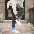 Model wearing blue gradient crew socks with white snowflakes, grey trousers, and white sneakers on a brick-paved sidewalk. [lf]
