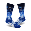 A pair of blue crew socks with a wintery design.  The socks feature white snowflakes and stylized trees on a blue and navy gradient background.