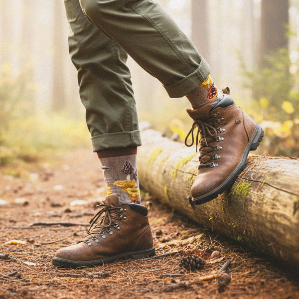 Model wears taupe mushroom crew sock, brown hiking boots, olive pants, stepping on a mossy log in a foggy forest. [lf]
