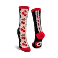 A pair of crew socks with a black background. One sock shows a line of red cherries with pale pink lace on the side. The other sock shows the heel and the cherry design.