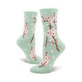 Pair of crew socks with a pastel green background, pink cherry blossoms, and falling petals design.