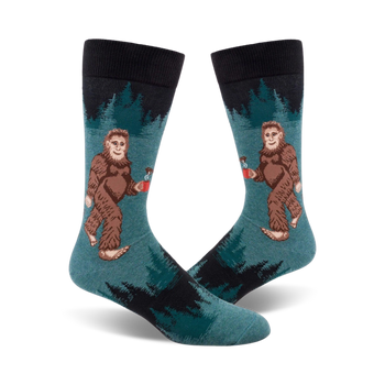 crew length socks in dark blue and teal feature cartoonish sasquatch holding coffee mugs surrounded by pine trees.  