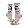 Crew socks in beige and grey featuring two raccoons peeking from a tree heart, with an arrow-pierced heart design at the bottom.