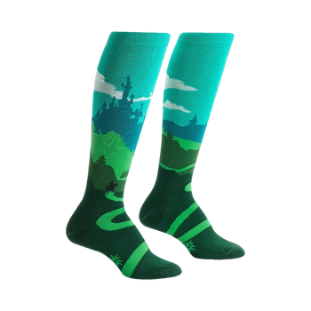 Pair of teal and green knee-high socks depicting a whimsical landscape with a castle, winding road, and a moose.