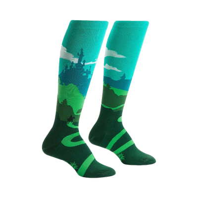 Pair of teal and green knee-high socks depicting a whimsical landscape with a castle, winding road, and a moose.